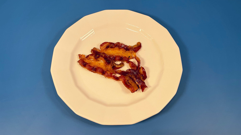 Two pieces of cooked Deen Halal bacon on a white plate and blue background