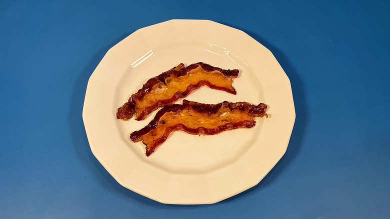 Two pieces of cooked Wellshire bacon on a white plate and blue background