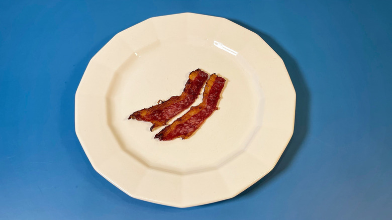 Two pieces of cooked Arnold's bacon on a white plate and blue background