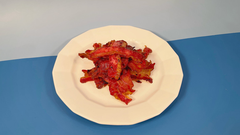 A white plate on a blue background piled high with cooked bacon