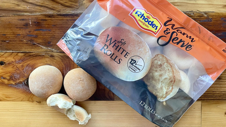 Three baked Rhodes Warm & Serve Soft White Rolls alongside bag of frozen ones