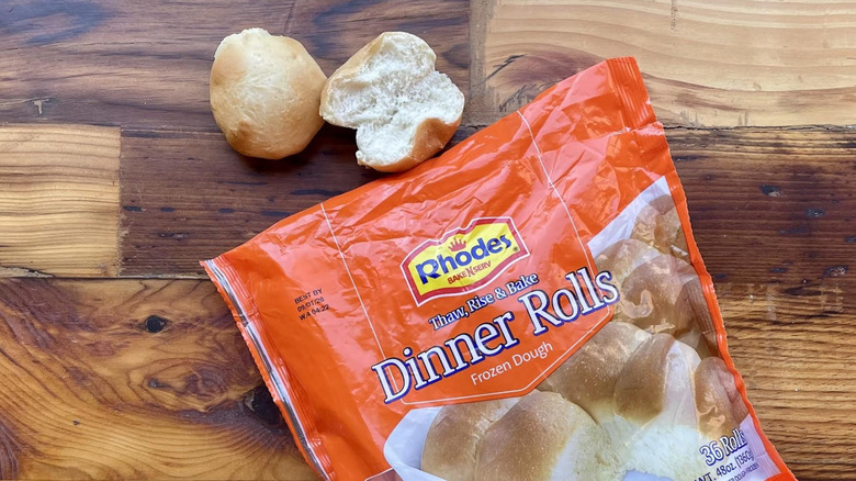 Two cooked Rhodes Dinner Rolls next to bag of frozen ones