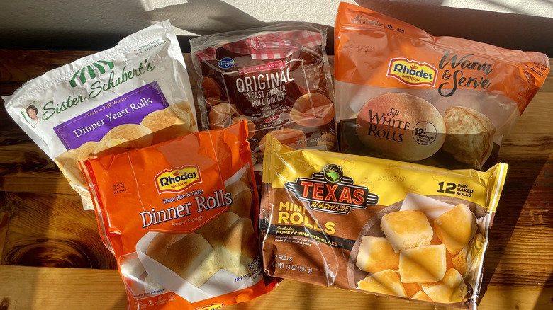 Five bags of different frozen store-bought dinner rolls on a sunny table