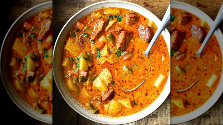 Spanish potato soup with various vegetables and chorizo on wood table.