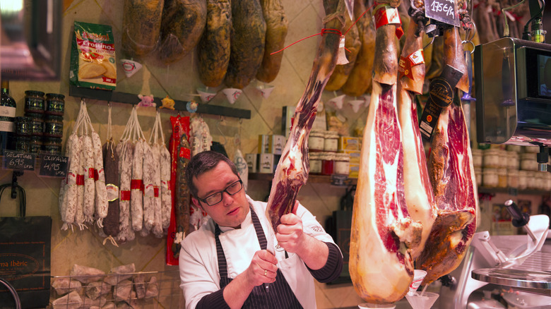 A butcher cutting a hanging piece of meat in a butcher shop