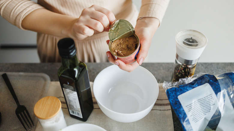 A person opening a can of tuna, with seasoning on the counter