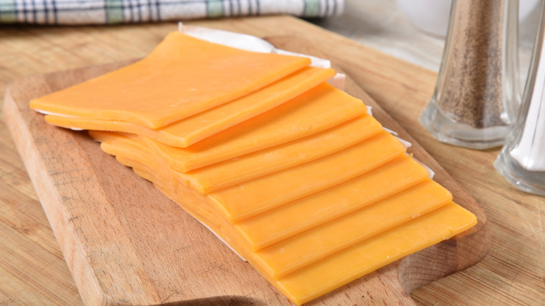 Sliced cheddar cheese on a wooden cutting board
