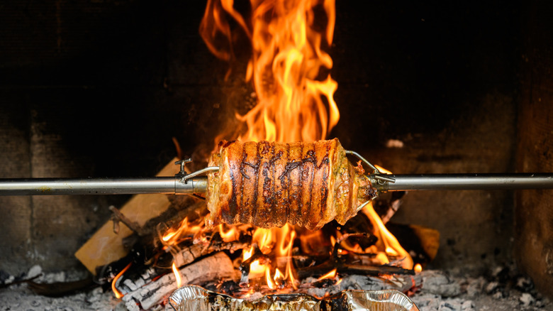 Twine wrapped meat being roasted over an open fire on a spit.