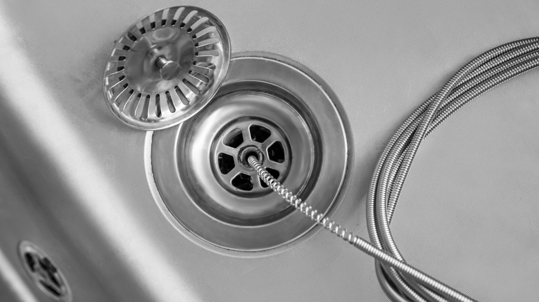 Kitchen sink drain with pipe snake pressed inside to unblock the drain.