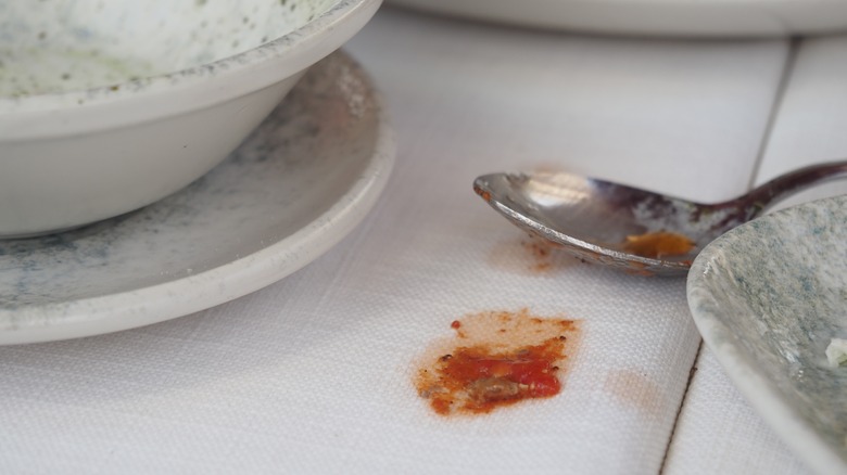 A tomato sauce stain spilled over a white cloth on a breakfast table.