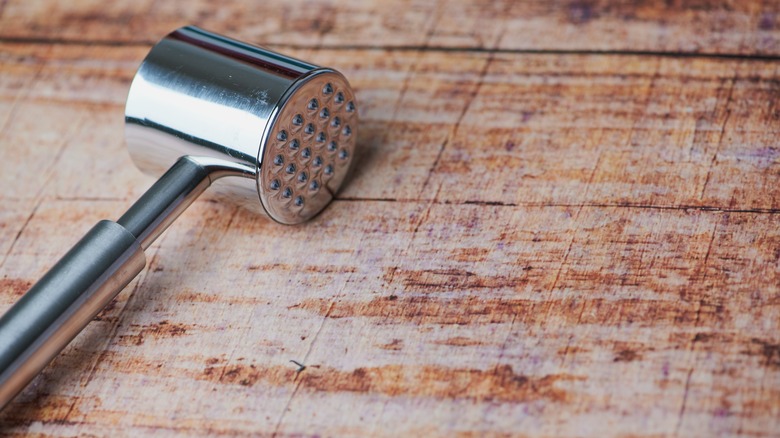 A meat tenderizer mallet on a wooden cutting board