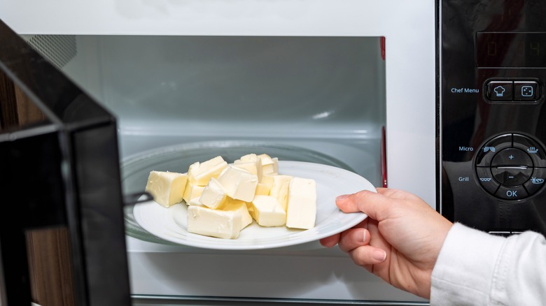 A hand placing a plate of butter into an open microwave