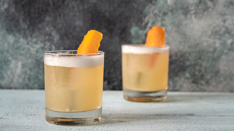 Two whiskey sour cocktails on a countertop.