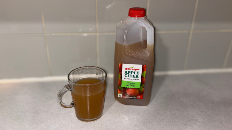 A clear mug 3/4 full of Giant Eagle 100% apple cider next to bottle of cider.