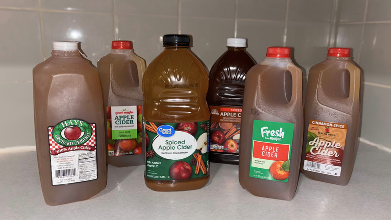 Six half-gallon jugs of apple cider sit on a counter.