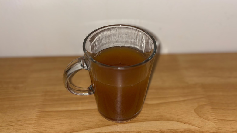 A glass mug 3/4 full of apple cider on a wooden table.