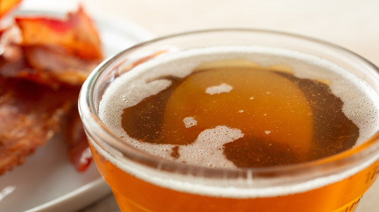 a close-up view of a glass bowl with bacon grease next to a plate of cooked bacon
