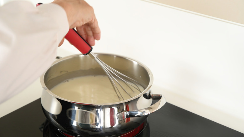 a chef scalding milk over the stovetop with a whisk