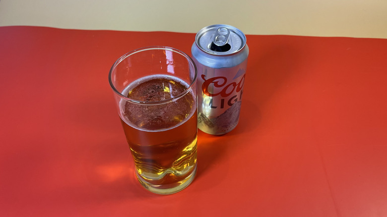A glass of Coors Light with the can on a red background