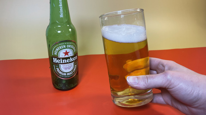 A hand holding a glass of Heineken next to the empty bottle