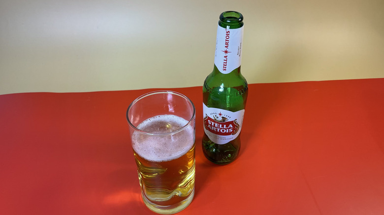 A glass of Stella Artois next to an empty bottle on a red background