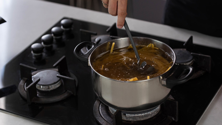 Person using a stainless steel pot on a gas stove
