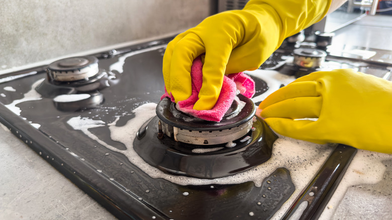 Person scrubbing a stove with gloves