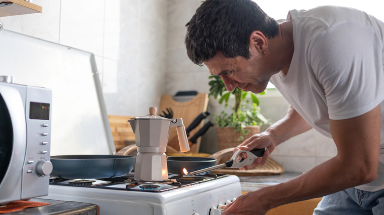 Person heating a pilot light on a stove with a moka pot