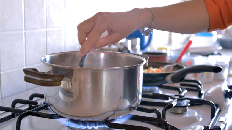Person stirring a pot on a gas stove