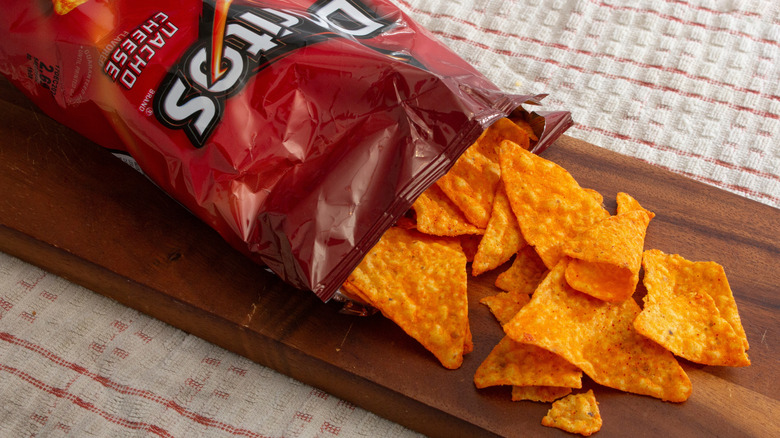 a bag of Doritos nacho cheese chips on its side with chips being poured out on a wooden slab