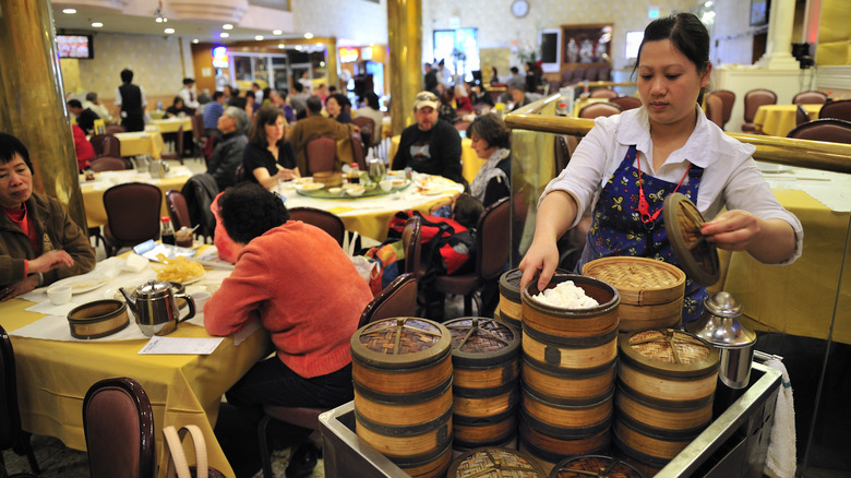 A bustling dim sum restaurant with a lady serving steamed buns