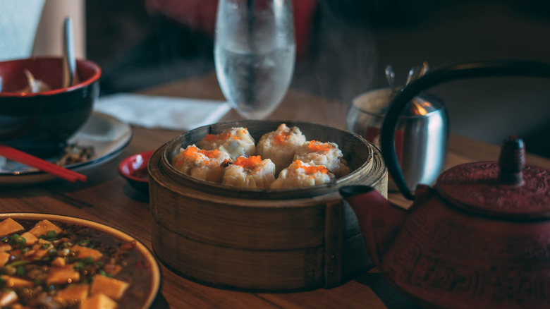 A basket of pork and shrimp siu mai alongside a bowl of mapo tofu and a tea pot