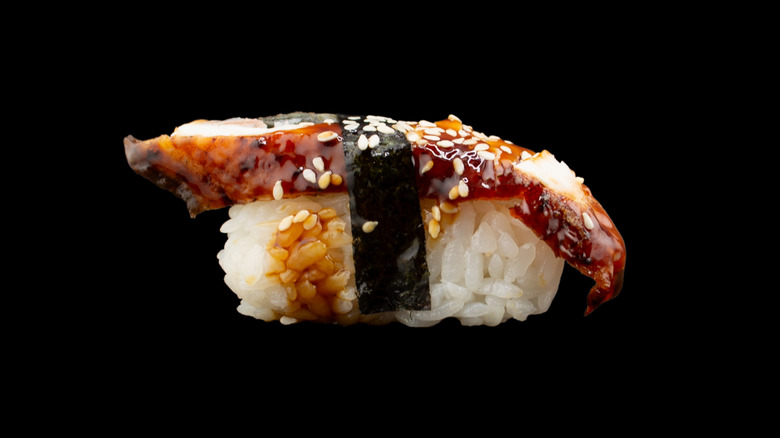 close-up shot of glazed eel nigiri wrapped in nori and coated in sesame seeds