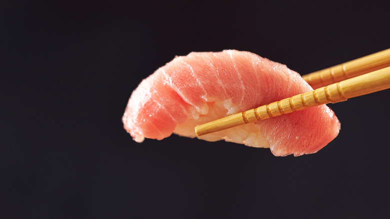 a piece of tuna nigiri in chopsticks with black background