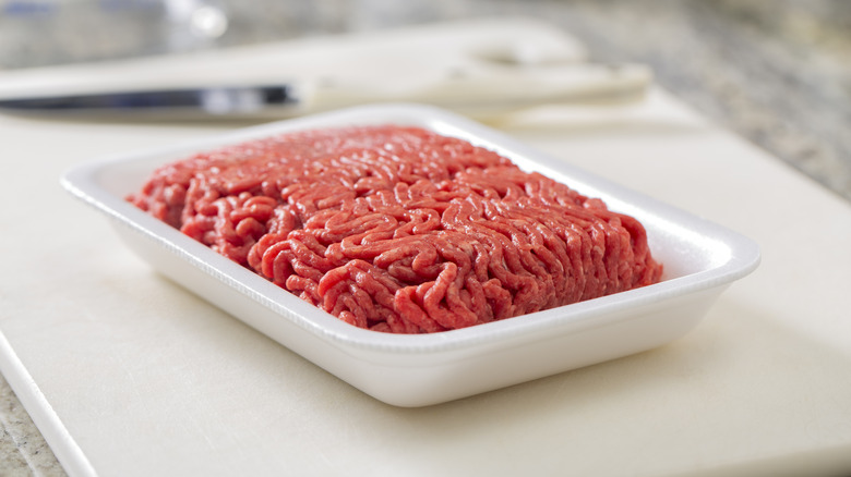 Ground beef sits in its packaging on a cutting board