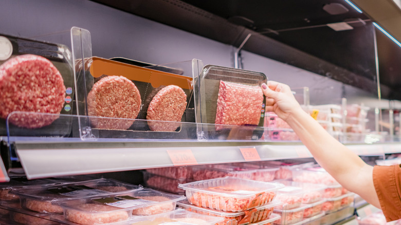 A shopper selects ground beef from the grocery store