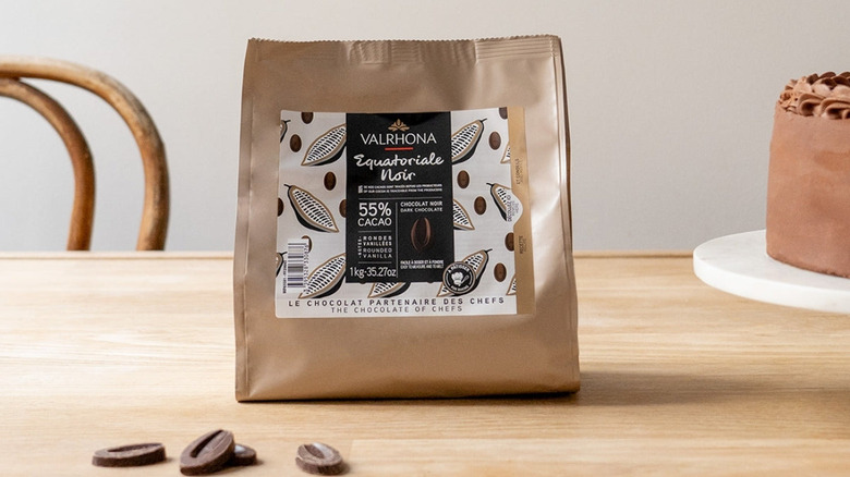 a bag of Valrhona Équatoriale Noire, 55% on a table with a few féves and a chocolate cake