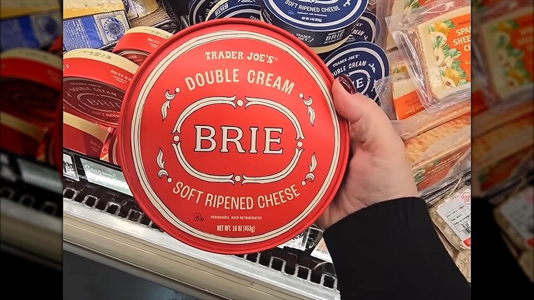 Hand holding Trader Joe's 16-ounce wheel of double cream brie cheese