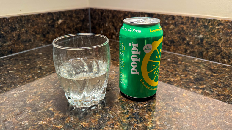 A can of Poppi lemon lime soda on a counter with a half-filled glass next to it