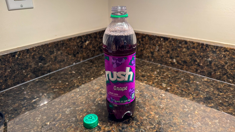 A bottle of Crush grape soda on a countertop with the cap removed