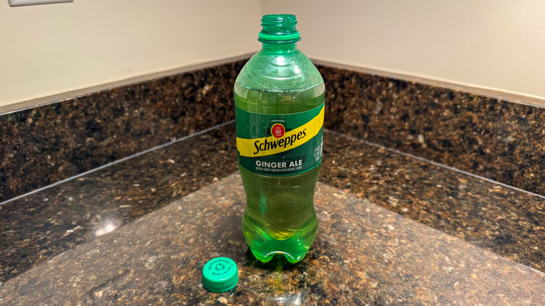 A Schweppes ginger ale bottle on a counter with the lid removed