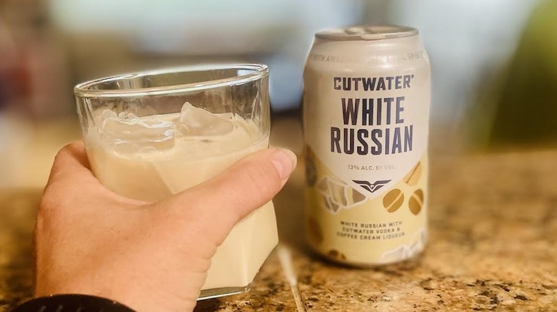 Hnad holding a glass of Cutwater Vodka White Russian with the can alongside