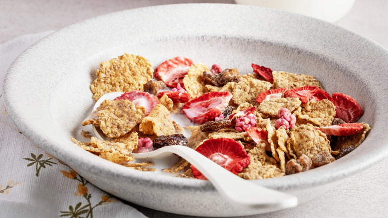A bowl of cereal with strawberries and a spoon