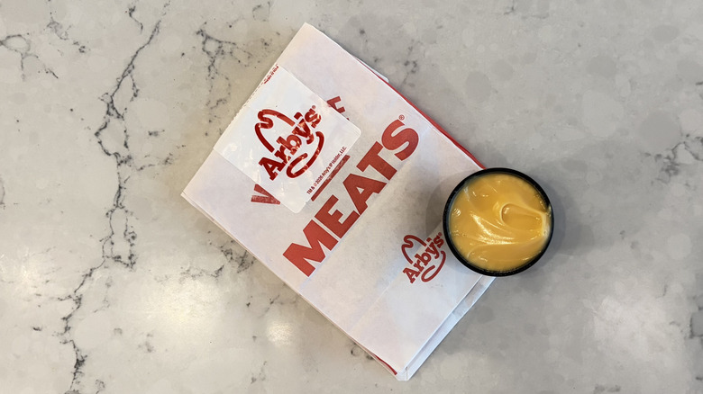A cup of Arby's Cheddar Cheese Sauce next to an Arby's bag