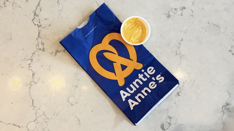 A cup of Auntie Anne's Cheese Dip next to an Auntie Anne's bag