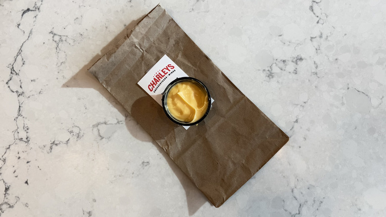 A cup of Charleys Cheesesteaks Cheese Sauce next to a Charleys Cheesesteaks bag