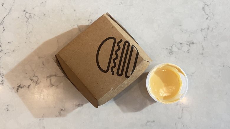 A cup of Shake Shack cheese sauce next to a Shake Shack box