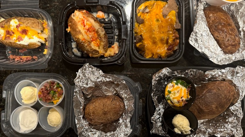 Overhead view of various loaded baked potatoes and toppings on black table
