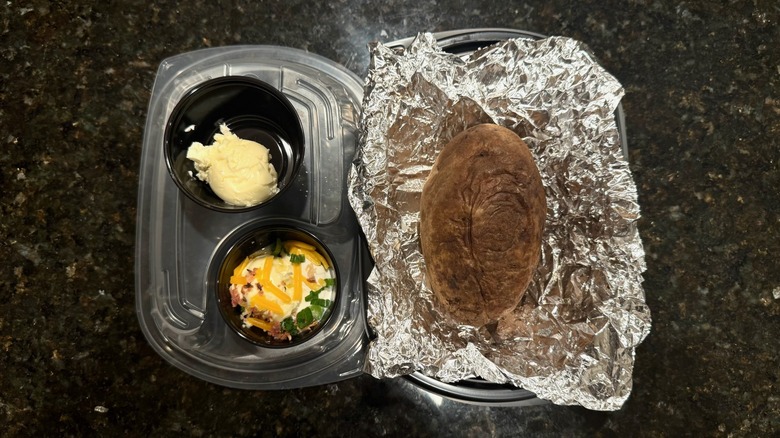 Takeout container with LongHorn Steakhouse baked potato and toppings on black table