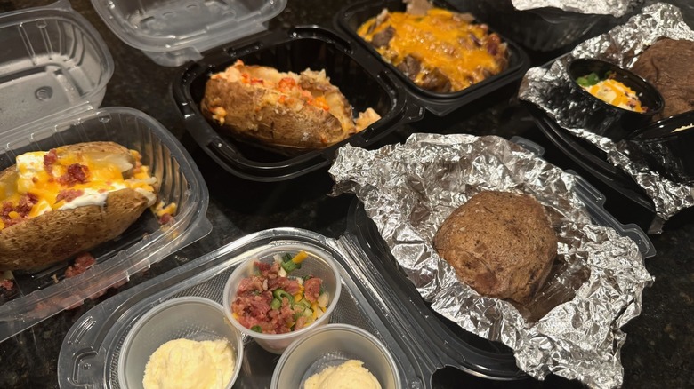 Various loaded baked potatoes in takeout containers on black table